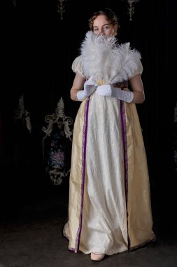 Gece kıyafeti giyen bir naip kadın, nakışlı bir elbise ve uzun bir spencer. Elinde büyük, beyaz bir devekuşu tüyü yelpazesi var.