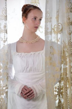 Beyaz pamuklu elbise giyen ve arkadan ışıklandırılmış dantel perdelerle çevrili bir naip kadın.