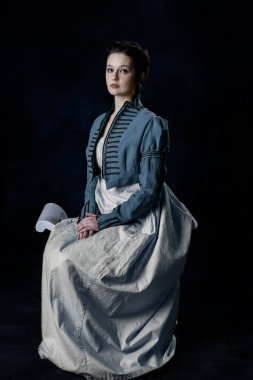 Mavi pamuklu bir elbise giyen naip bir kadın ve tahta koltukta oturan kısa saçlı bir Spencer.