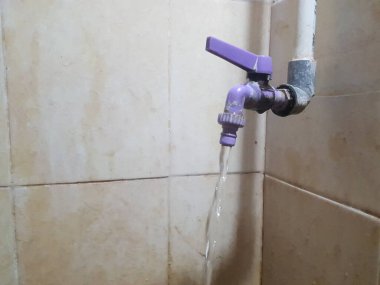 Suyu akan mor bir musluk, bej renkli bir duvara monte edilmiş.