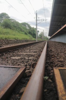 Çakıl taşlı, yeşil ve bulutlu gökyüzü ile çevrili bir demiryolu hattının alçak açılı görüntüsü.