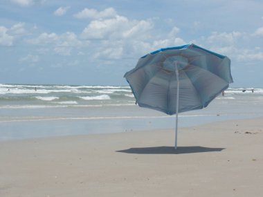 A lone blue umbrella in the sand at New Smyrna Beach Florida on a sunny Spring Day clipart