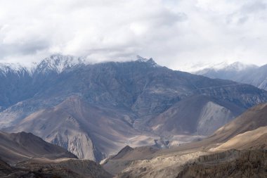 Nepal 'in Mustang Bölgesi' nin güzel çölü ve arka planda karla kaplı dağlar alçak bulut örtüsüyle.