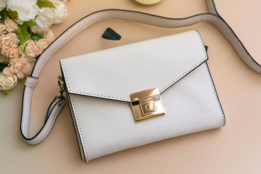 Beyaz çiçekli beyaz çanta ve bej arka planda bir el çantası.