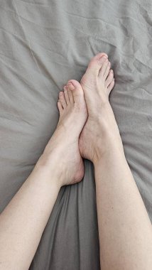 Gri çarşaflarda kadınların ayakları birbirine yaslanır. Dikey fotoğrafçılık