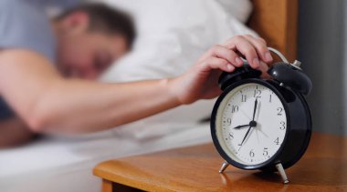 Yorgun bir adam yatak odasındaki çalar saat tarafından uyandırılıyor. Yüksek kalite fotoğraf