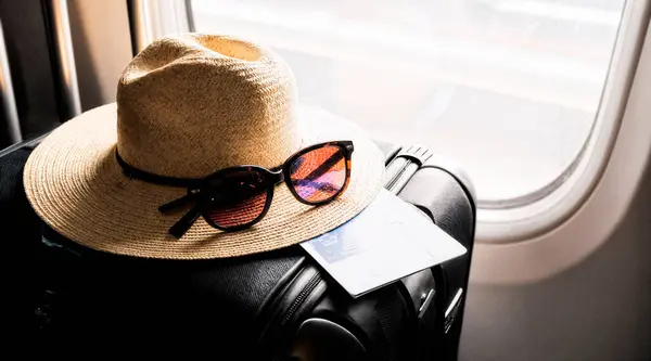 Bir biniş kartı, güneş gözlüğü ve pencerenin yanındaki bir bavulun üzerine yerleştirilmiş hasır bir şapka. Yüksek kalite fotoğraf