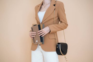  Bej arka planda kahverengi ceketli bir kız elinde defterler tutuyor. Yüksek kalite fotoğraf