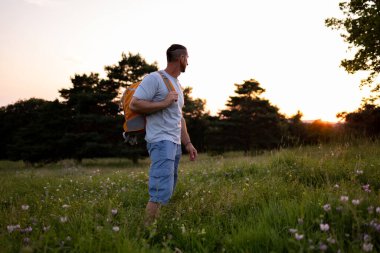 Omuzlarında sırt çantasıyla bir erkek turist çayırda gün batımını bekliyor. Yüksek kalite fotoğraf