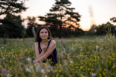 Güzel, genç, hayalperest kız doğada oturuyor ve elinde bir buket kır çiçeği tutuyor. Yüksek kalite fotoğraf