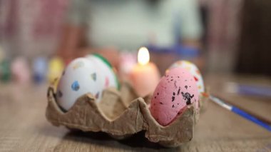 Katılımcılar yumurtaları çeşitli renklerde ve tasarımlarla sıcak, davetkar bir yere boyuyorlar. Her yerde fırça ve canlı boya gibi aletler var, neşeli atmosferi güçlendiriyor..