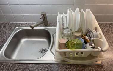 Temiz tabaklar, bardaklar ve çatal bıçak takımı paslanmaz çelik lavabonun yanındaki rafta dinleniyor. Mutfak ortamını düzenliyor ve bulaşıkları yıkıyor..