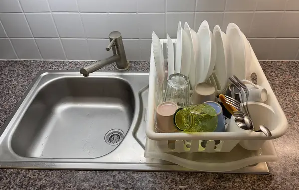 Temiz tabaklar, bardaklar ve çatal bıçak takımı paslanmaz çelik lavabonun yanındaki rafta dinleniyor. Mutfak ortamını düzenliyor ve bulaşıkları yıkıyor..
