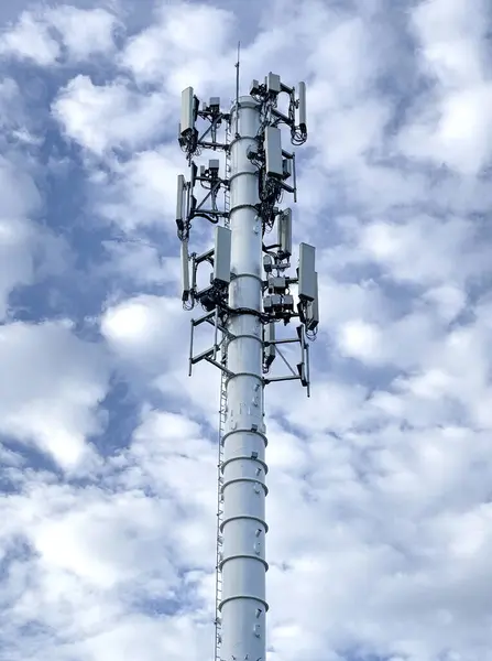 stock image Modern cell phone tower equipped with multiple antennas and transmitters stands tall against a partly cloudy blue sky. This infrastructure plays a crucial role in providing wireless communication services.