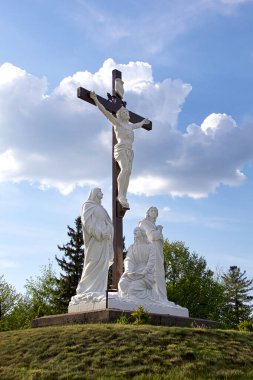 İsa 'nın çarmıha gerilmesinin çarpıcı açık hava heykeli, etrafını dindar figürlerle çevrili, dinsel figürler, dinsel bir gökyüzü ve yemyeşil bir zemin üzerine kurulmuş