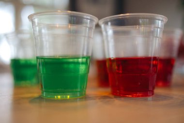 Ahşap bir masada iki fincan jöle - biri yeşil renkli ve biri kırmızı renkli, diğer bardakların önünde istiflenmiş.