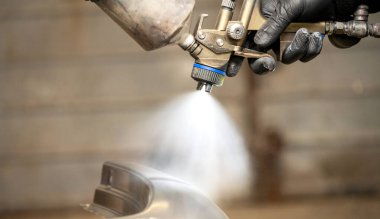 Close-up image of a skilled worker's gloved hands using a professional spray gun to paint a car part, highlighting the precision spray and fine mist. clipart