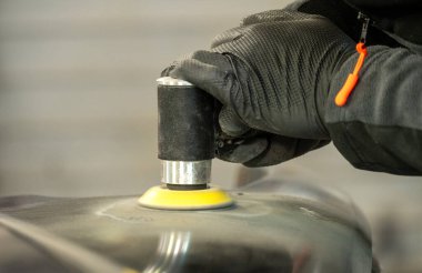 Yetenekli bir oto tamircisi yörünge cilası kullanarak arabanın kaputunu cilalar, dikkatle aracın parlaklığına odaklanır ve çizikleri temizler..