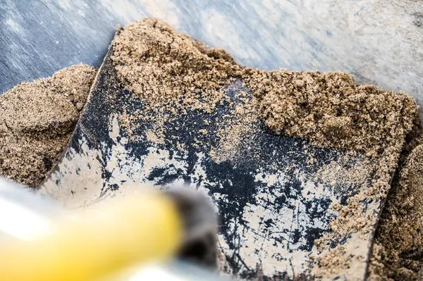 Stock image Detailed view of a rusty metal shovel lifting sand, highlighting texture contrasts between rust and fresh sand. Ideal for construction or gardening themes.