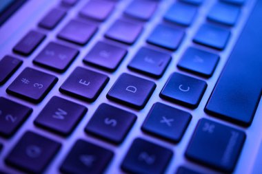 Mavi ışık altında modern bir dizüstü bilgisayarın klavyesinin yakın plan görüntüsü, insan etkileşimi olmadan her anahtarın dokusunu ve detaylarını vurguluyor.