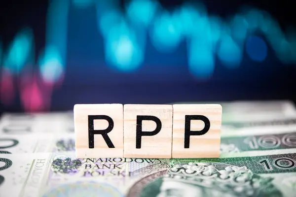 stock image Close-up view of wooden alphabet blocks spelling 'RPP', arranged on Polish z?oty currency, illuminated by ethereal blue bokeh lights. Represents monetary concepts or financial policy.