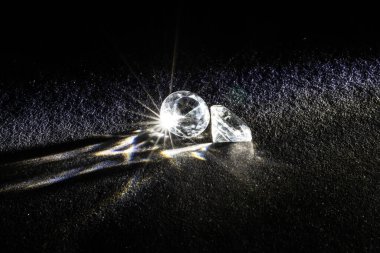 Karanlık bir yüzeyde uzanan göz kamaştırıcı iki elmasın yakın çekim görüntüsü parlak ışık ışınlarını parlak parıltılarla yansıtıyor. Bu resim değerli taşların güzelliğini ve lüksünü gösteriyor..