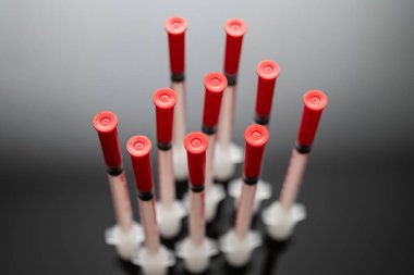 Dikey olarak hizalanmış birkaç kan örneği tüpünün yakından görüntüsü kırmızı başlıklarla tam olarak tıbbi araştırma ve test amaçlı koyu bir yansıtıcı yüzeyde düzenlenmiştir..