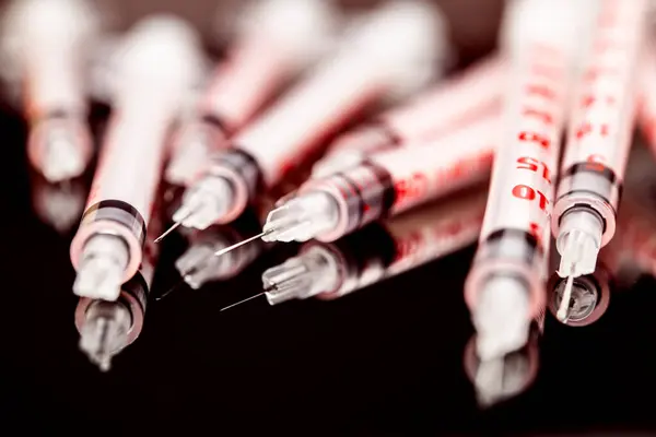 stock image This photograph captures an array of medical insulin syringes closely packed together on a dark, reflective surface, highlighting their sharp needles and measurement markings.