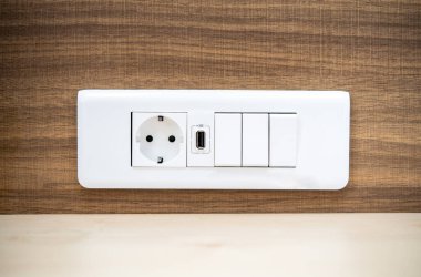 Modern bir elektrik prizinin detaylı görüntüsü USB bağlantı noktası ve ahşap bir duvardaki ışık düğmeleri ile birleştirilmiş. Ev yenileme ve modern iç tasarım kavramları için ideal..