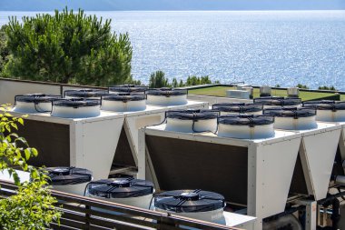 Geniş ticari havalandırma üniteleri çatıda, stratejik olarak uygun hava sirkülasyonu ve soğutma verimliliği için yerleştirilmiş. Sakin bir denize bakan, endüstriyel teknolojiyle doğal güzelliği birleştiren. Sürdürülebilirlik ve enerji temaları için ideal