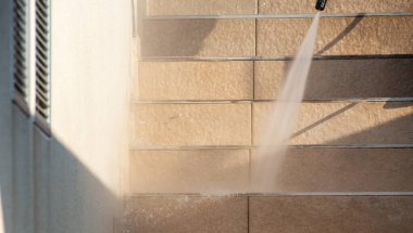 Yüksek basınçlı temizlik işlemi, bej döşemeli bir duvara su püskürterek, güneşli kentsel ortamda etkin açık hava temizleme tekniklerini gösteren bir hortum püskürterek bir eylemin ortasında kaydedildi..