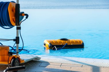 Açık mavi bir havuzda güneşli bir günde çalışan otomatik bir robotik havuz temizleyicisini çeken canlı bir fotoğraf. Modern ev bakım teknolojisini sergilemek için mükemmel..