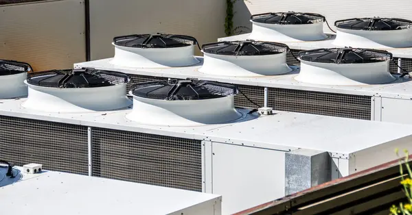 stock image Multiple industrial air conditioning units installed on a commercial building's roof, showcasing urban infrastructure and modern HVAC technology. White and black cooling units, highlighting functionality and design in commercial settings.