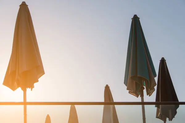 stock image Sunset at a serene beach captured with multiple closed umbrellas lined against a soft, glowing sky. The image evokes a peaceful, tranquil evening at a seaside, perfect for themes of relaxation and vacation.