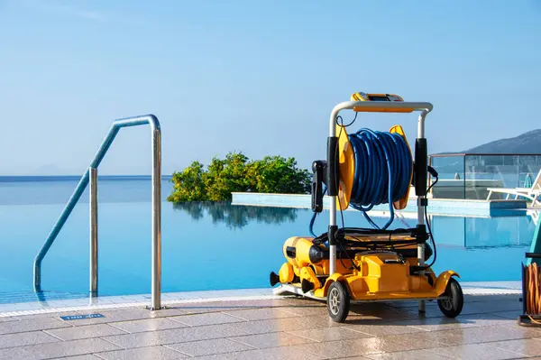 stock image Robotic pool cleaner stationed on sunny terrace beside an infinity pool overlooking the sea. Perfect for maintaining crystal-clear water in luxury pools.