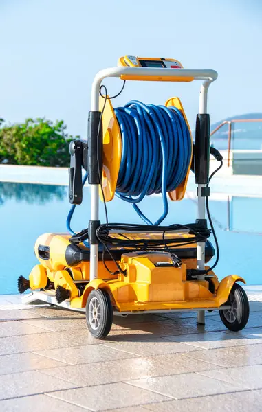 stock image A modern, automated robotic pool cleaner equipped with hoses and reels, parked on a cart beside a clear, blue swimming pool. Ideal for showcasing pool cleaning technology and luxury lifestyle.