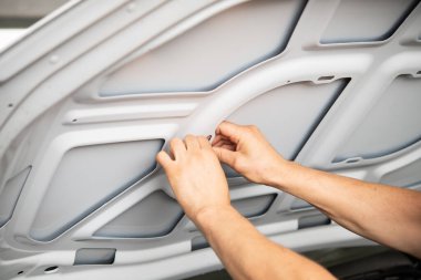 Odaklanmış bir birey araba kaputu içinde bakım yapıyor, uygun olması için panelleri ayarlıyor, araç bakımında otomotiv onarım becerileri ve detaylara dikkat gösteriyor.