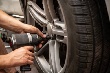 Yetenekli bir teknisyen, tekerleği kış veya yaz lastiğiyle takmak için İngiliz anahtarı kullanır. Mevsimsel lastik değiştirme ve otomotiv bakımı için gereken hassasiyeti vurgular..