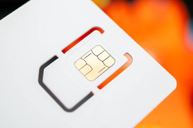 Sim kartın yüksek çözünürlüklü yakın çekimi, altın çip dizaynlı, bulanık turuncu arka plan üzerine kurulmuş. Telekomünikasyon, mobil teknoloji ve dijital iletişim temaları için mükemmel.