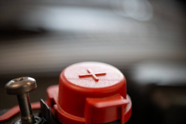 Otomotiv bakım ve mühendisliğini temsil eden artı işaretli kırmızı pil kapağının ayrıntılı yakın çekimi, mekanik temayı geliştiren odaksız motor arkaplanı.