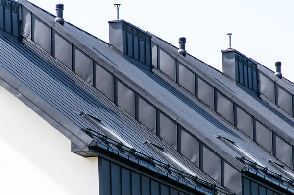 stock image Stylish metallic roofs with windows and ventilation, reflecting contemporary architectural trends in residential housing against a bright, clear sky.