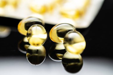 D vitamini ve Omega 3 balık yağı içeren saydam sarı kapsüller. Yansıtıcı bir yüzey ve su toplayan kapsüllere karşı sergilenen kapsüller, sağlık ve besinleri destekliyor.