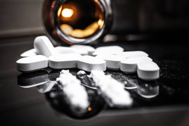 Parlak bir yüzeye dağılmış reçeteli opioid tabletlerinin yakın görüntüsü ve pudralanmış fentanil, opioid kullanımı ve bağımlılığıyla ilişkili riskleri vurguluyor.