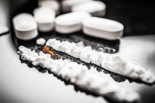 A close-up view of white pills alongside fentanyl powder, emphasizing the relationship between prescription drugs and the opioid crisis affecting many individuals in society.