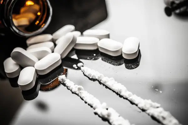 Reçeteli opioidler ve fentanil tozu yansıtıcı bir yüzeye dağılmış durumda, uyuşturucu kullanımının tehlikelerini ve bireyleri ve toplulukları etkileyen devam eden opioid krizini göstermektedir..