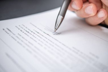 Odaklanmış bir birey, ofis ortamında sorumluluk ve profesyonelliği vurgulayan gümüş kalemle yasal bir belge imzalıyor..