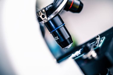 Bir örneği hedef alan mikroskop merceğine yakından bakmak, klinik bir ortamda laboratuvar araştırmaları ve bilimsel çalışmalar için karmaşık tasarımı ve işlevselliğini vurgulamak.