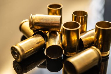 Yansıtıcı yüzeydeki mermi kovanlarının yakın çekim görüntüsü. Bu resim ateşli silahları, mühimmatı, atış sporlarını, nişancılığın ve atış taliminin dinamik doğasını simgeler..