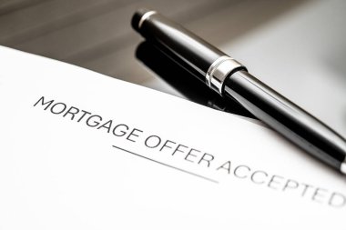 Emlak işlemlerini, mali onayları, ev satın almayı ve yatırım fırsatlarını sembolize eden, modern bir masanın üzerindeki parlak kalemlerin yanına kabul edilmiş bir mortgage teklifi belgesi.
