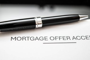 Potansiyel ev sahipleri ve alıcılar için gerekli olan ev satın alma, mali planlama ve gayrimenkul işlemlerini gösteren, siyah kalemin yanında bir ipotek teklifi kabul belgesinin ayrıntılı yakın plan çizimi.